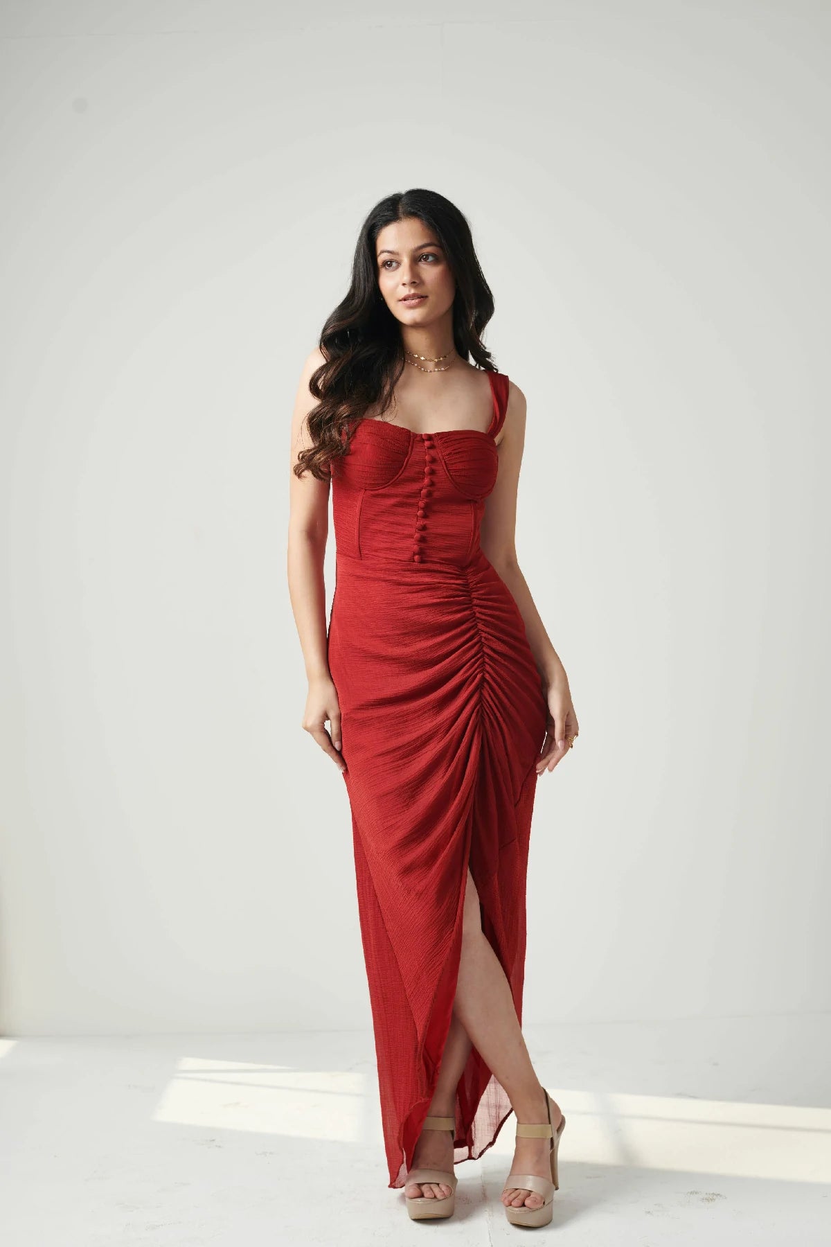 A woman wearing a red chiffon dress with front gather details and a side slit.